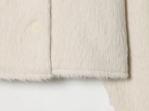Macro view of plush oat-white knit jacket hem showing button detail and fluffy mohair texture