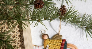 Detail of painted metal angel ornament hanging on pine branches for Christmas decor