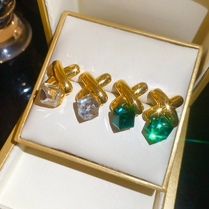 Close-up of golden X-shaped earrings with clear and emerald cube crystals in a jewelry box