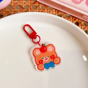Detail of cute acrylic bear keychain with red apple hat and blue bow on a ceramic plate