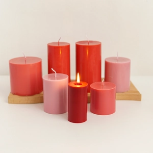 Collection of various pink and red cylindrical aroma candles on a wooden tray with flame