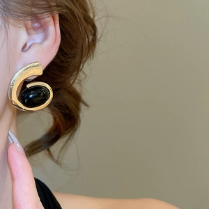 Detailed close-up of a model wearing a gold-tone geometric earring with a black oval stone