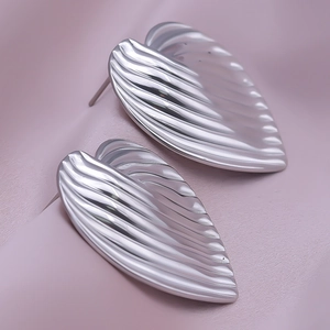 Macro detail of silver leaf earrings with pleated texture on silk background