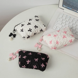 Quilted bow makeup bags with 3D texture and pearl pendant on a desk with a laptop
