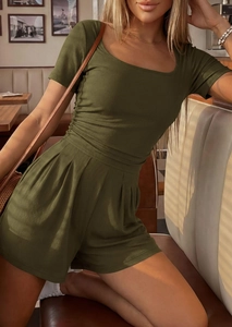 Detail of dark green knit short jumpsuit featuring ribbed texture and pleated waistline