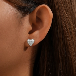 Close-up of heart-shaped silver earrings with sparkling stones on model's ear