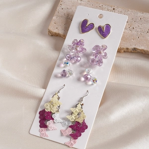 Detailed set of purple heart studs, flower beads, and butterfly drop earrings on silk