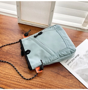 Detail of light blue nylon crossbody bag with orange drawstring on wooden surface