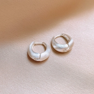 Macro shot of minimalist matte silver earrings on soft champagne silk fabric