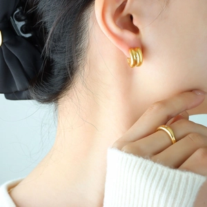 Detail of double-layered C-shaped gold-plated stud earrings and ring worn by model
