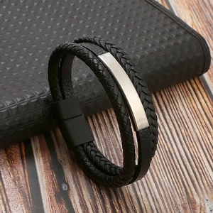 Detail of black braided leather bracelet with silver metal plate on a wooden surface