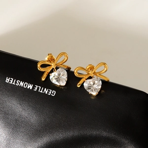 Golden bow stud earrings with heart-shaped zircon drop on black textured background