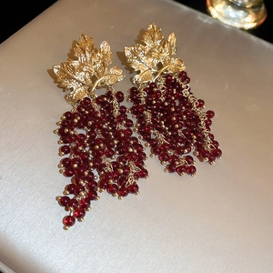 Macro detail of leaf-shaped gold base and red grape cluster bead tassels on drop earrings