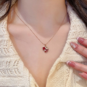 Detailed close-up of a golden gourd pendant necklace with red zircon on a female model
