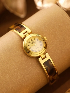 Close-up of a gold women's watch featuring a tortoise shell link chain and small round dial