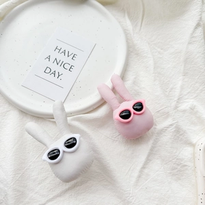 Close-up of white and pink plush rabbit phone grips with sunglasses in a cozy setting
