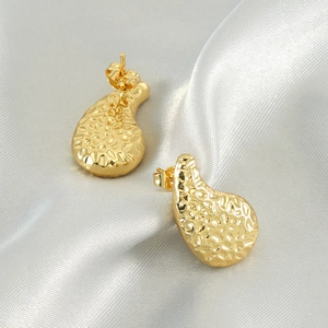 Golden hammer textured teardrop earrings in irregular shape on silver silk background
