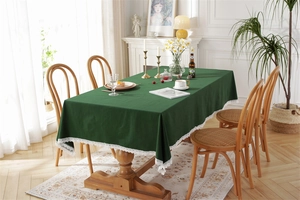 Green cotton tablecloth with white lace edges on a wooden dining table in a cozy room