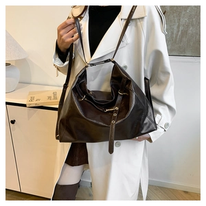 Detail of a large dark brown polished leather tote bag with adjustable straps and metal buckles