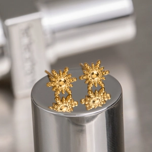 Star earrings and sunflower studs in golden stainless steel set on a reflective cylinder