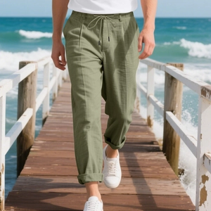 Pantalon droit en lin vert sauge pour homme porté dans un décor de plage décontracté