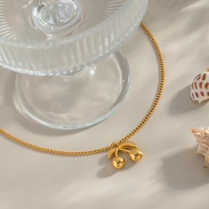 Macro detail of 18K gold cherry pendant necklace with polished finish on beige surface