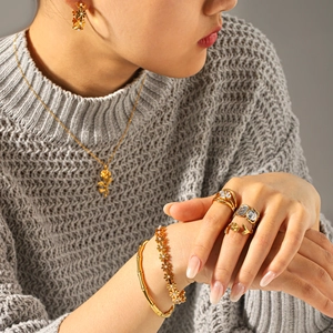 Golden rose jewelry set with necklace earrings and rings on a grey sweater background