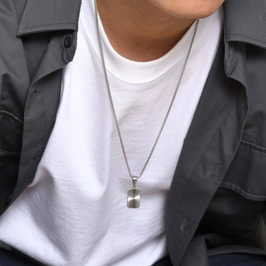 Close-up of men's silver rectangular pendant with radiant sun texture on a steel chain