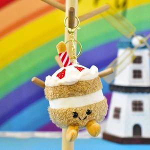 Detailed view of a cake plush keychain with a strawberry topping and a smiley face