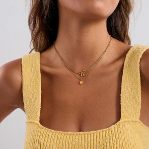 Detail of double-layer gold necklace featuring bow and heart pendants on a model