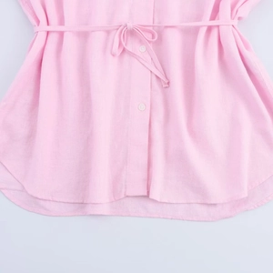 Detail of pink cotton-linen shirt featuring textured fabric, waist tie, and white buttons