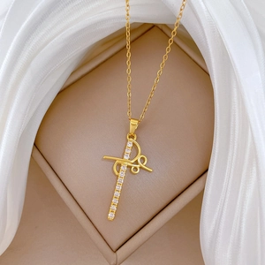 Macro shot of gold cross necklace with R-letter detail and crystals on silk fabric