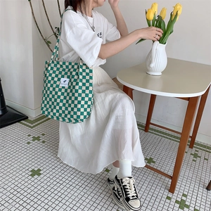 Detail of green and beige checkered corduroy tote bag worn by a model in a cozy setting