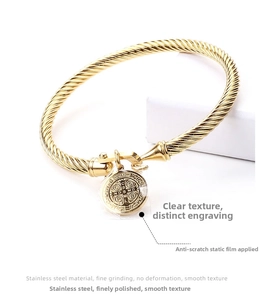 Detailed close-up of a gold-plated twisted cable bracelet with a St. Benedict coin charm