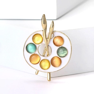 Luxurious gold artist palette brooch with colorful opals and two brushes on white backdrop