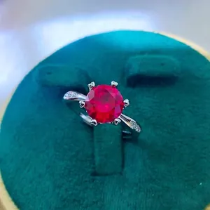 Detail of round cut ruby ring featuring six-prong setting on silver band with side stones