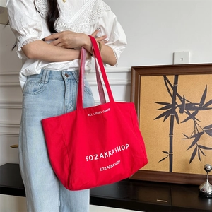 Detailaufnahme der roten Segeltuchtasche mit weißer Aufschrift und Streifenriemen