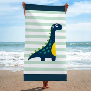 Cartoon dinosaur print beach towel with blue and green stripes shown on a sunny beach