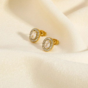 Detail of gold oval stud earrings with clear gemstone inlay on beige silk fabric