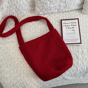 Vue à plat d'un sac seau rouge en polaire pelucheuse sur un tapis de laine blanche