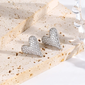 Detail of silver heart-shaped stud earrings with pave zircon on beige stone surface