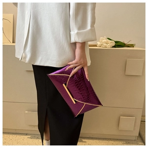 Detail of purple crocodile texture envelope clutch bag with gold metallic trim and magnetic clasp