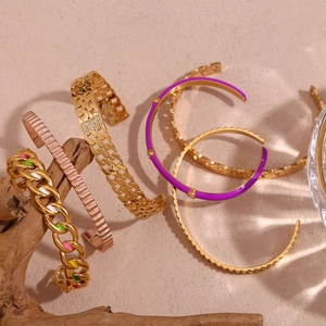 Close-up of gold and rose gold chain bracelets with enamel bangles on a natural wood stand