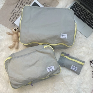 Close-up of three gray plaid travel organizer bags with contrast yellow zippers on white rug