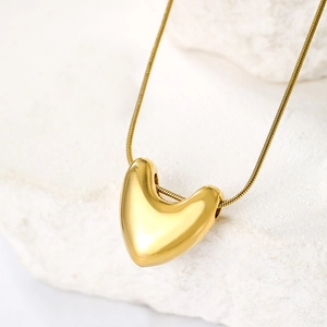 Detail of 3D gold heart pendant on a sleek snake chain over a white stone base