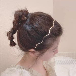 Elegant gold wavy metal headband for women worn by a model in a minimalist setting