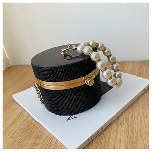 Close-up of black rhinestone cylinder evening bag with large pearl handle and gold trim