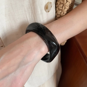 Detailed view of a wide acrylic bangle with black marble pattern on a woman's wrist