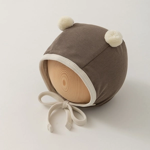 Close-up of baby earflap hat in coffee brown with cream pom-poms and adjustable straps