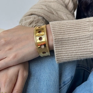 Detail of wide gold hollow cuff bracelet with woven texture on a female wrist